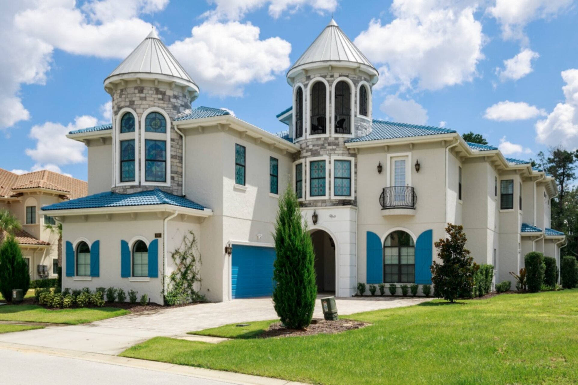 Exterior of a luxury Orlando villa featuring white stone turrets, blue tiled roofing, and Mediterranean architectural details under a clear sky.