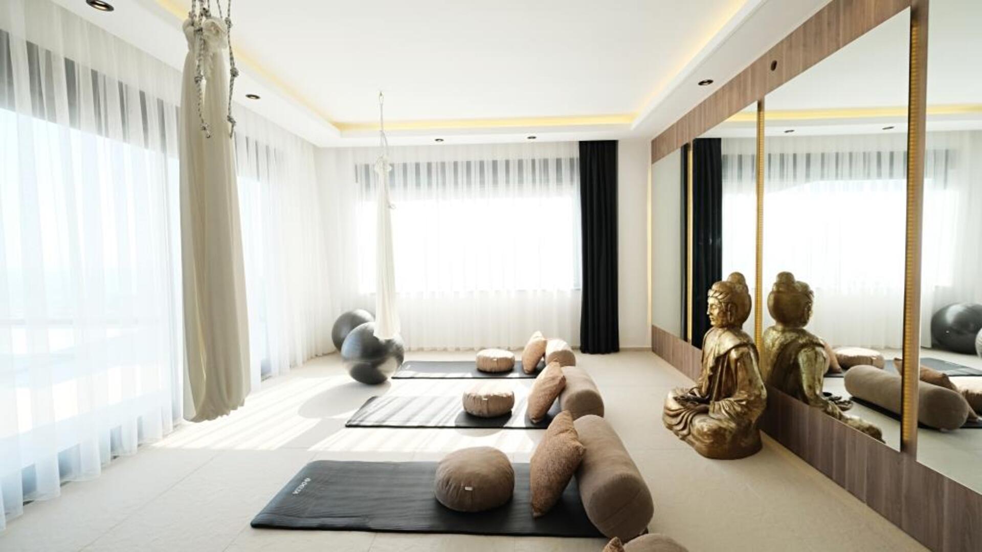 The private yoga studio at Alanya Holiday Villa -5 Star Infinity Villa, featuring aerial silk hammocks, meditation cushions, and a large Buddha statue in a sun-lit, mirrored room.