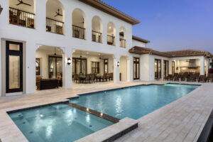 An expansive illuminated private pool and outdoor living area of a luxury villa at Reunion Resort, featuring white arched architecture and multiple lounge areas under a dusk sky.