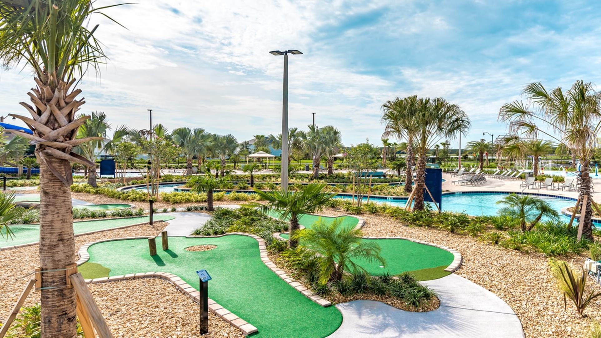 A bright, outdoor amenity area at Storey Lake Resort in Orlando, featuring a green mini-golf course in the foreground and a blue lazy river pool winding through palm trees in the background
