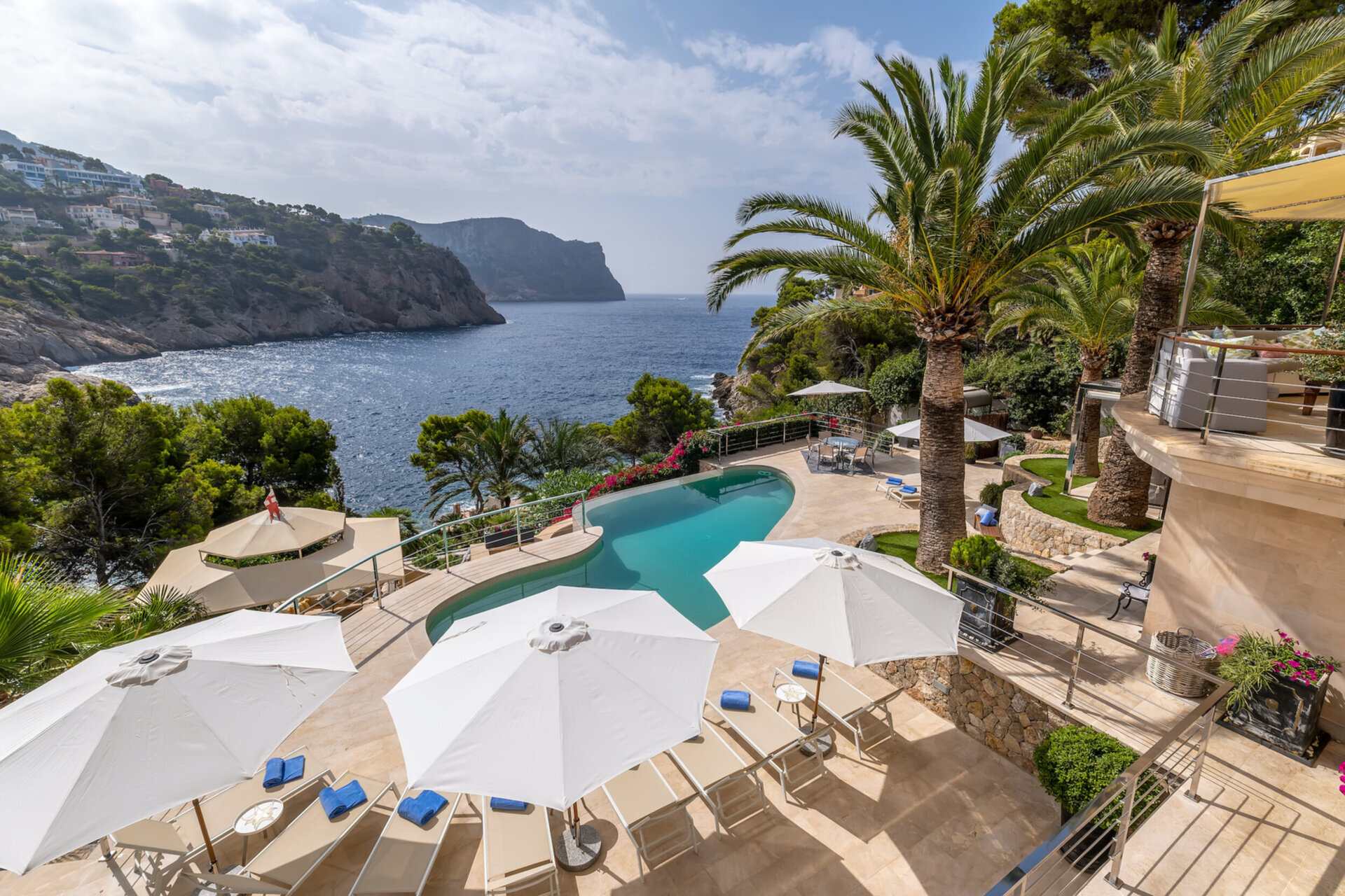 Aerial view of a luxury Mallorca villa pool area overlooking a turquoise bay, featuring white parasols and a private sun deck for quiet luxury.