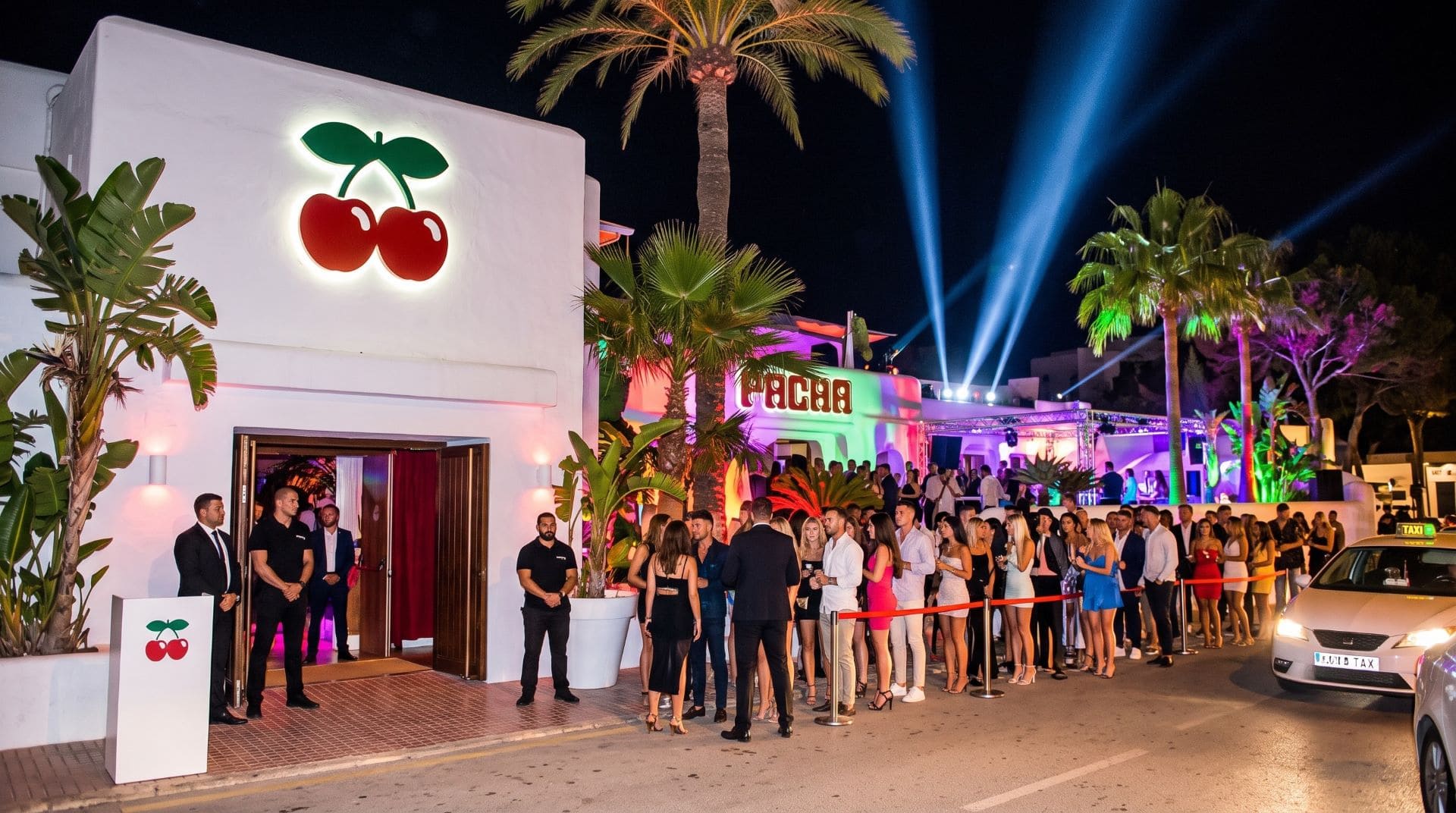 Crowds queuing outside Pacha nightclub in Ibiza at night, with lit-up sign and entrance